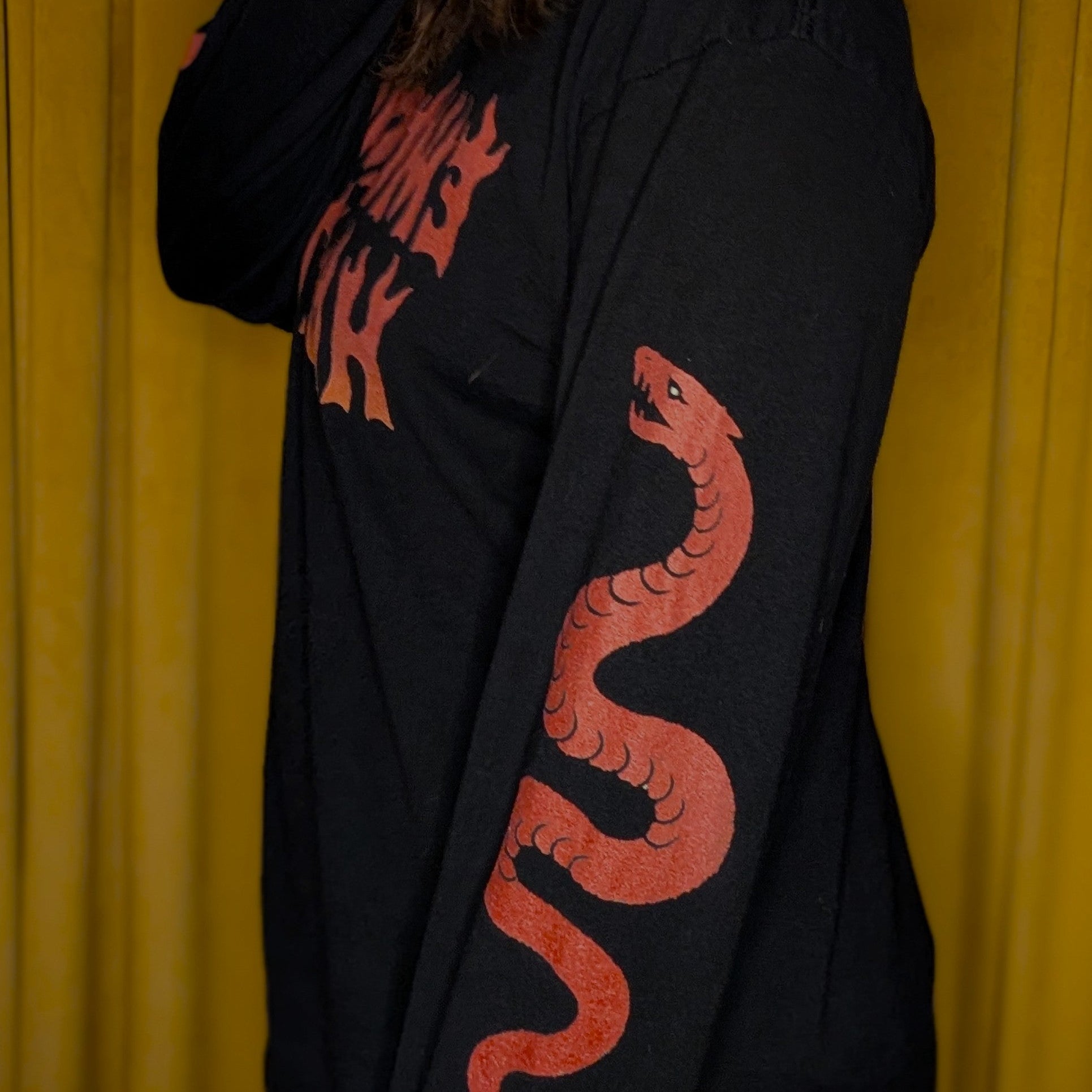 Black long-sleeve shirt with red snake design against a yellow curtain background